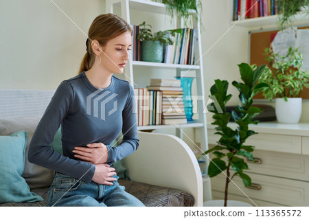 Young teenage female experiencing abdominal pain, sitting on couch at home 113365572