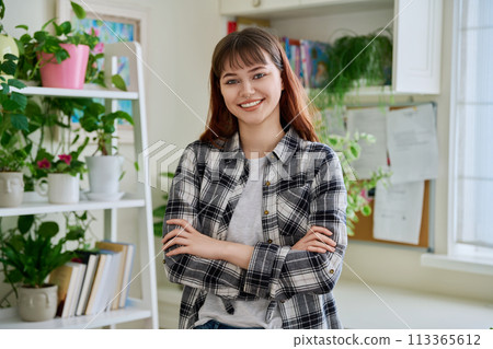 Portrait of smiling female teenager looking at camera with crossed arms in home 113365612