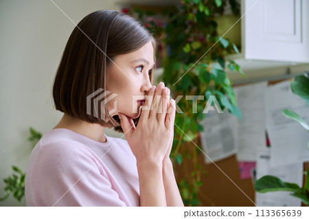 Profile view close-up of young woman's face with hands folded in prayer, dreams 113365639