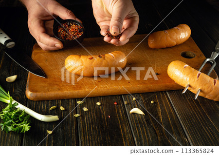 Preparation for grilling on the kitchen table with Vienna sausages by the hands of a chef. Grill cooking concept with sausages and aromatic spices. European cuisine Preparation for grilling on the kitchen table with Vienna sausages by the hands of a chef. Grill cooking concept with sausages and aromatic spices. European cuisine 113365824