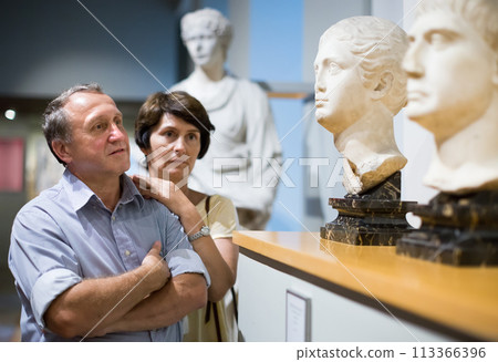 Mature couple turists examines the exhibit in museum 113366396