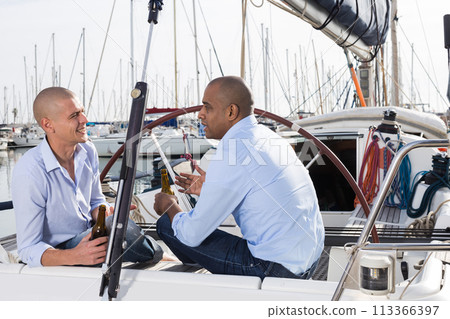 Two men in blue shirts sitting on sailing yacht in the port 113366397
