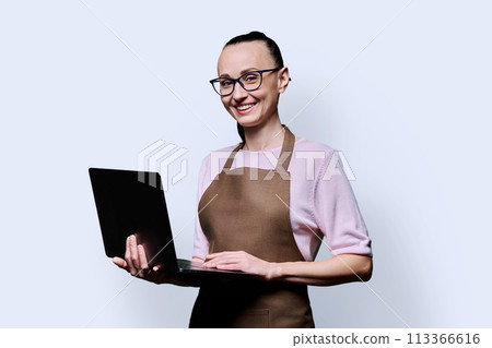 Portrait of 30s woman in apron holding laptop on blue background 113366616