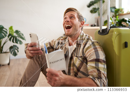 Happy young man with passport, tickets and smartphone, laughing, sitting with suitcase, going on vacation Happy young man with passport, tickets and smartphone, laughing, sitting with suitcase, going on vacation 113366933