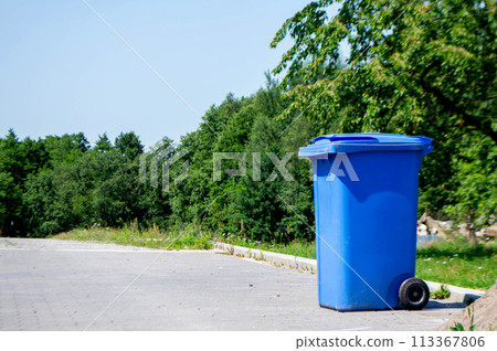Unloocked big empty blue plastic trash garbage bin in front of the modern house with green trees. No public trash on the side of the road. Infectious control, garbage disposal of waste concept Unloocked big empty blue plastic trash garbage bin in front of the modern house with green trees. No public trash on the side of the road. Infectious control, garbage disposal of waste concept 113367806