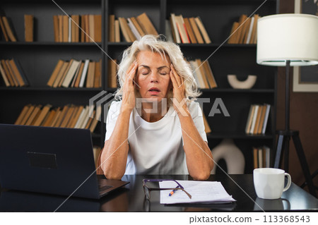 Headache pain. Middle aged woman touching temples experiencing stress. Mature old lady tired of work feeling headache sick rubbing temples forehead. Long laptop usage computer vision office syndrome Headache pain. Middle aged woman touching temples experiencing stress. Mature old lady tired of work feeling headache sick rubbing temples forehead. Long laptop usage computer vision office syndrome 113368543