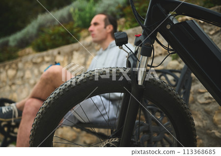 Selective focus on tubeless tire of an electric motor bike, mountain bike over blurred background of male cyclist in the city 113368685