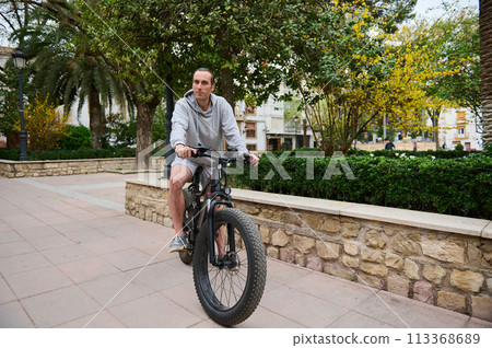 Full length portrait of a sportsman renting, riding modern ecologically friendly electric bike in the city 113368689