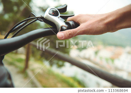 Close-up man cyclist puts hands on brakes, squeezing then while descending during his trip on electric bike in the mountains. 113368694