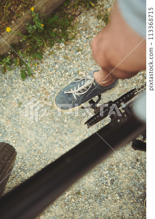 Cyclist point of view. Close-up top view of male foot in denim sneakers on the electric bike pedal, riding outdoors Cyclist point of view. Close-up top view of male foot in denim sneakers on the electric bike pedal, riding outdoors 113368715