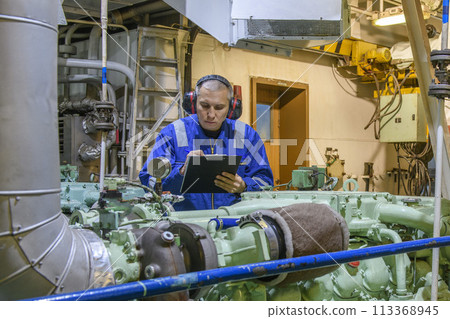 Marine Engineer in blue overall working in Engine room of ship. Work at sea. Motorman. 113368945