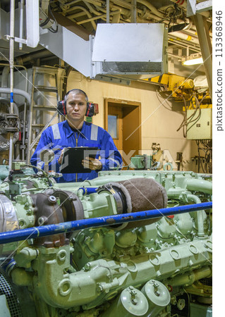 Marine Engineer in blue overall working in Engine room of ship. Work at sea. Motorman. 113368946