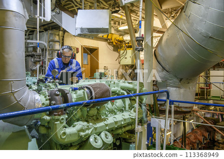 Marine Engineer in blue overall working in Engine room of ship. Work at sea. Motorman. 113368949