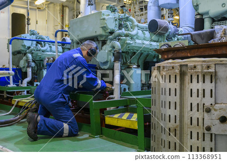Engineer in blue overall doing service of generator in Engine room of vessel. Work at sea.  Motorman. 113368951