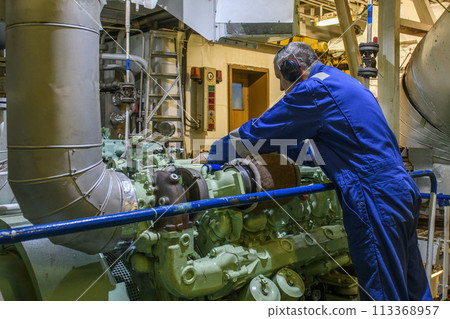 Marine Engineer in blue overall working in Engine room of ship. Work at sea. Motorman. 113368957