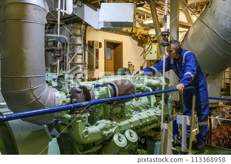 Marine Engineer in blue overall working in Engine room of ship. Work at sea. Motorman. 113368958
