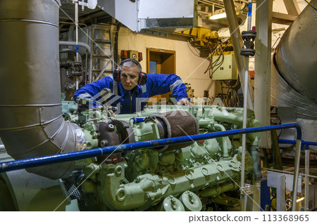 Marine Engineer in blue overall working in Engine room of ship. Work at sea. Motorman. 113368965