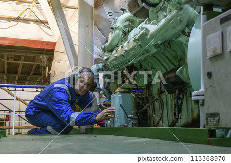 Marine Engineer in blue overall working in Engine room of ship. Work at sea. Motorman. 113368970