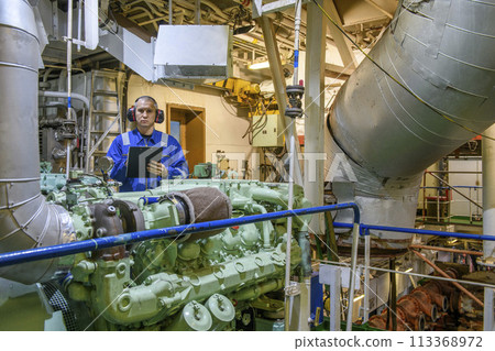 Marine Engineer in blue overall working in Engine room of ship. Work at sea. Motorman. 113368972