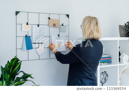 Back view middle aged businesswoman pinning work-life balance wheel diagram on grid mood board on her work space. Finding Balance in Your Life. Life planning. Coaching tools. Selective focus. Back view middle aged businesswoman pinning work-life balance wheel diagram on grid mood board on her work space. Finding Balance in Your Life. Life planning. Coaching tools. Selective focus. 113369554