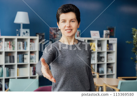 Polite friendly middle aged neutral gender hr manager recruiter posing for portrait looking at camera stretching hand to spectator proposing handshaking inviting for job interview welcoming in office. Polite friendly middle aged neutral gender hr manager recruiter posing for portrait looking at camera stretching hand to spectator proposing handshaking inviting for job interview welcoming in office. 113369580