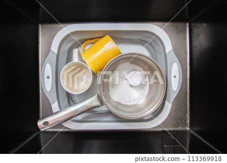 measuring spoon with granules of environmentally friendly oxygen bleach in a basin with dirty dishes. Cleaning grease and dirt from dishes, close-up 113369918