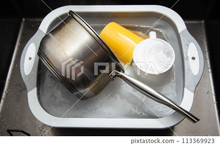 Dirty dishes in a sink basin with hot water and foam from an environmental oxygen cleaner. A modern product for removing dirt and stains. 113369923