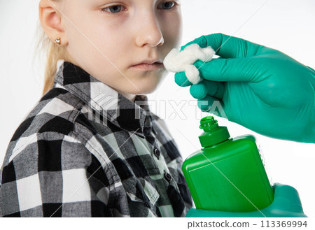 a doctor's hand in a medical glove holds a cotton swab with ammonia to the nose of a seven-year-old girl. Concept of presyncope and syncope in children, close-up 113369994