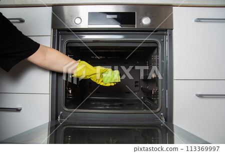 A girl holds a sponge in her hand against the background of an oven. Concept for cleaning electric ovens in the kitchen, cleaning company. Washing up A girl holds a sponge in her hand against the background of an oven. Concept for cleaning electric ovens in the kitchen, cleaning company. Washing up 113369997