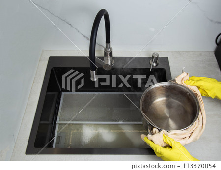 Man's hands in yellow gloves pour pots of hot water into a sink with dirty filters from the hood in the kitchen. Cleaning from dirt and grease with an oxygen cleaner. Copy space for text 113370054