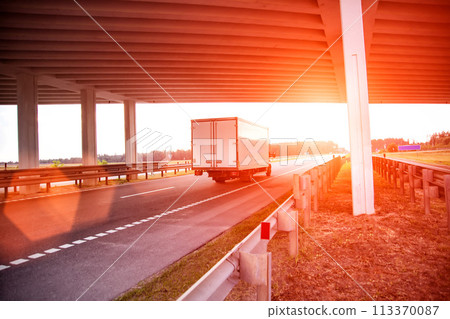A red light-duty refrigerated van transports perishable cargo on the highway in the summer against the backdrop of sunset, industry 113370087