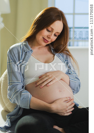 Pregnancy motherhood people expectation future. Pregnant woman touching big belly sitting on couch at home. Girl hugging her tummy enjoying pregnancy. Maternity tenderness parenthood new life concept 113370088