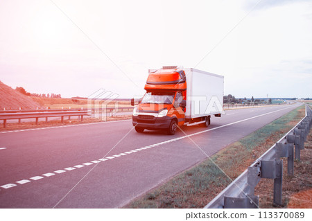 A red light-duty refrigerated van transports perishable cargo on the highway in the summer against the backdrop of sunset, industry A red light-duty refrigerated van transports perishable cargo on the highway in the summer against the backdrop of sunset, industry 113370089