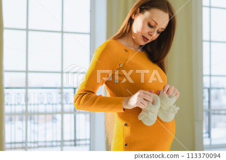 Pregnancy motherhood people expectation future. Pregnant woman with big belly holding newborn baby booties smiling at home. Young mom enjoying pregnancy. Maternity tenderness parenthood new life Pregnancy motherhood people expectation future. Pregnant woman with big belly holding newborn baby booties smiling at home. Young mom enjoying pregnancy. Maternity tenderness parenthood new life 113370094