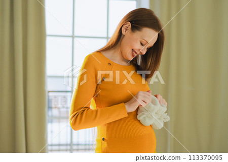 Pregnancy motherhood people expectation future. Pregnant woman with big belly holding newborn baby booties smiling at home. Young mom enjoying pregnancy. Maternity tenderness parenthood new life Pregnancy motherhood people expectation future. Pregnant woman with big belly holding newborn baby booties smiling at home. Young mom enjoying pregnancy. Maternity tenderness parenthood new life 113370095