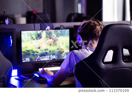 Serious focused teen gamer in headset playing PC video game at computer club during cyber sport tournament. E-sport championship. Modern multiplayer online real-time strategy RTS, tactics skill Serious focused teen gamer in headset playing PC video game at computer club during cyber sport tournament. E-sport championship. Modern multiplayer online real-time strategy RTS, tactics skill 113370109