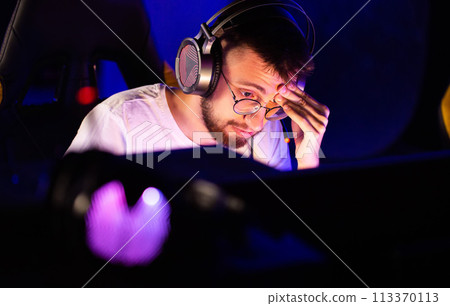 Adult bristly gamer in glasses headset plays video game on PC, player moves his eyes, computer club cyber sport tournament. E-sport championship. Multiplayer online first-person shooter, strategy Adult bristly gamer in glasses headset plays video game on PC, player moves his eyes, computer club cyber sport tournament. E-sport championship. Multiplayer online first-person shooter, strategy 113370113