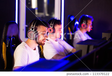 Gamers team playing video game on PC at cyber club during E-sport championship, rack focus from computers to players in headset, sport tournament. Multiplayer online strategy RTS tactical shooter 113370122
