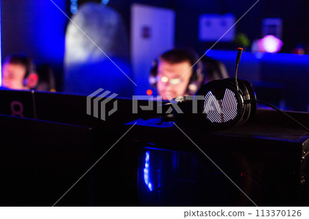 Headphones in focus in a computer club with players in the background. Concept of a tournament and playing computer games. Copy space for text 113370126