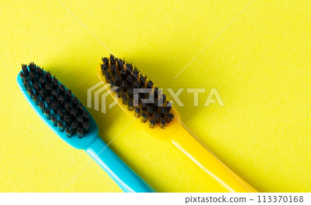 Two toothbrushes with black charcoal hard bristles on a yellow background, close-up. The concept of hygiene and teeth cleaning in dentistry, macro. Copy space for text. View from above 113370168