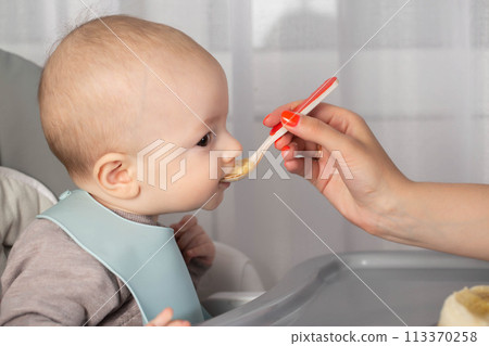 Feeding porridge and puree of a small child from a spoon. First meal. Copy space for text 113370258