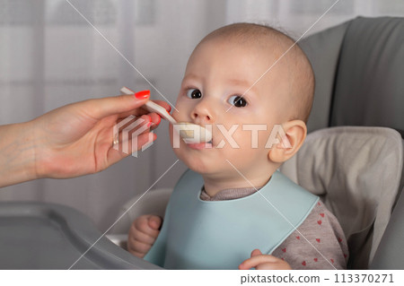 A mother feeds a baby boy who is 8 months old with meat puree. Feeding an infant. Close-up, copy space for text 113370271