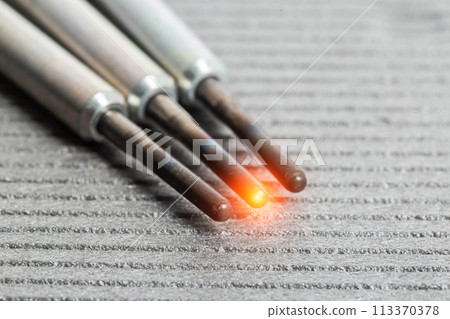 Serviceable modern ceramic glow plugs on a gray background. Orange glow, heating element. Pre-heating of a diesel engine, close-up 113370378