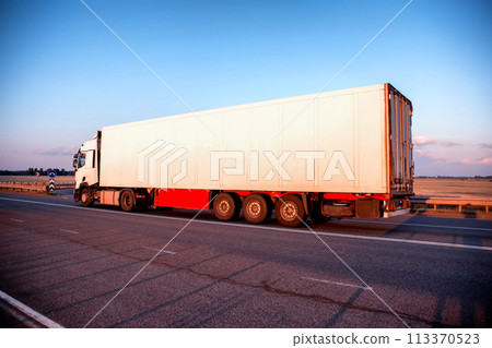 A truck with a refrigerated semi-trailer transports perishable food products in the evening against a blue sky. Import substitution, delivery of medicines, industry. 113370523