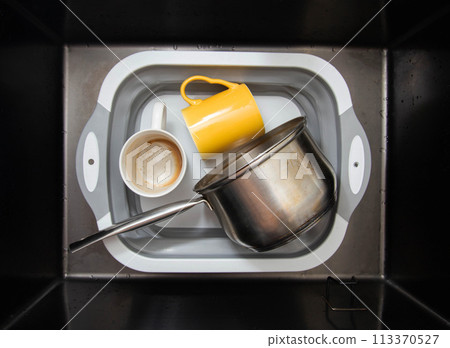 A basin in the sink with dirty dishes, mugs and a saucepan. Cleaning grease stains using environmentally friendly oxygen bleach. 113370527