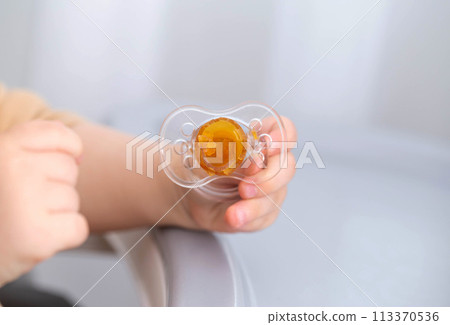 The baby is holding a torn and chewed silicone pacifier in his hands. Concept of teething in children, sucking reflex. Copy space for text The baby is holding a torn and chewed silicone pacifier in his hands. Concept of teething in children, sucking reflex. Copy space for text 113370536