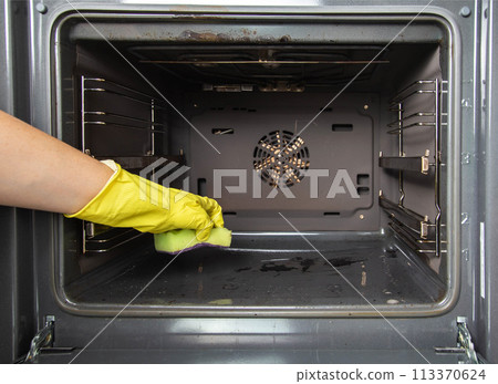A girl holds a sponge in her hand against the background of an oven. Concept for cleaning electric ovens in the kitchen, cleaning company. Washing up A girl holds a sponge in her hand against the background of an oven. Concept for cleaning electric ovens in the kitchen, cleaning company. Washing up 113370624