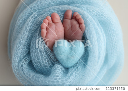 The tiny foot of a newborn baby. Soft feet of a new born in a blue wool blanket. Close up of toes, heels and feet of a newborn. Knitted blue heart in the legs of a baby. Macro photography.  113371350