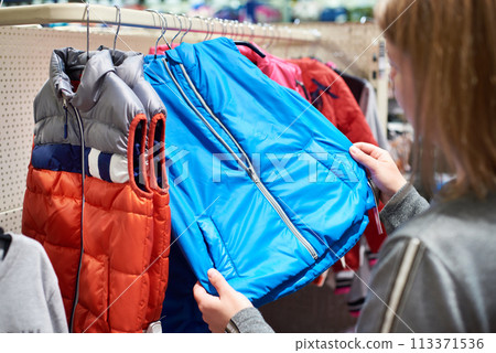 Buyer woman chooses waistcoat clothes in store 113371536