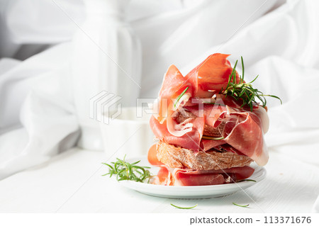 Ciabatta with prosciutto and rosemary on a white wooden table. 113371676